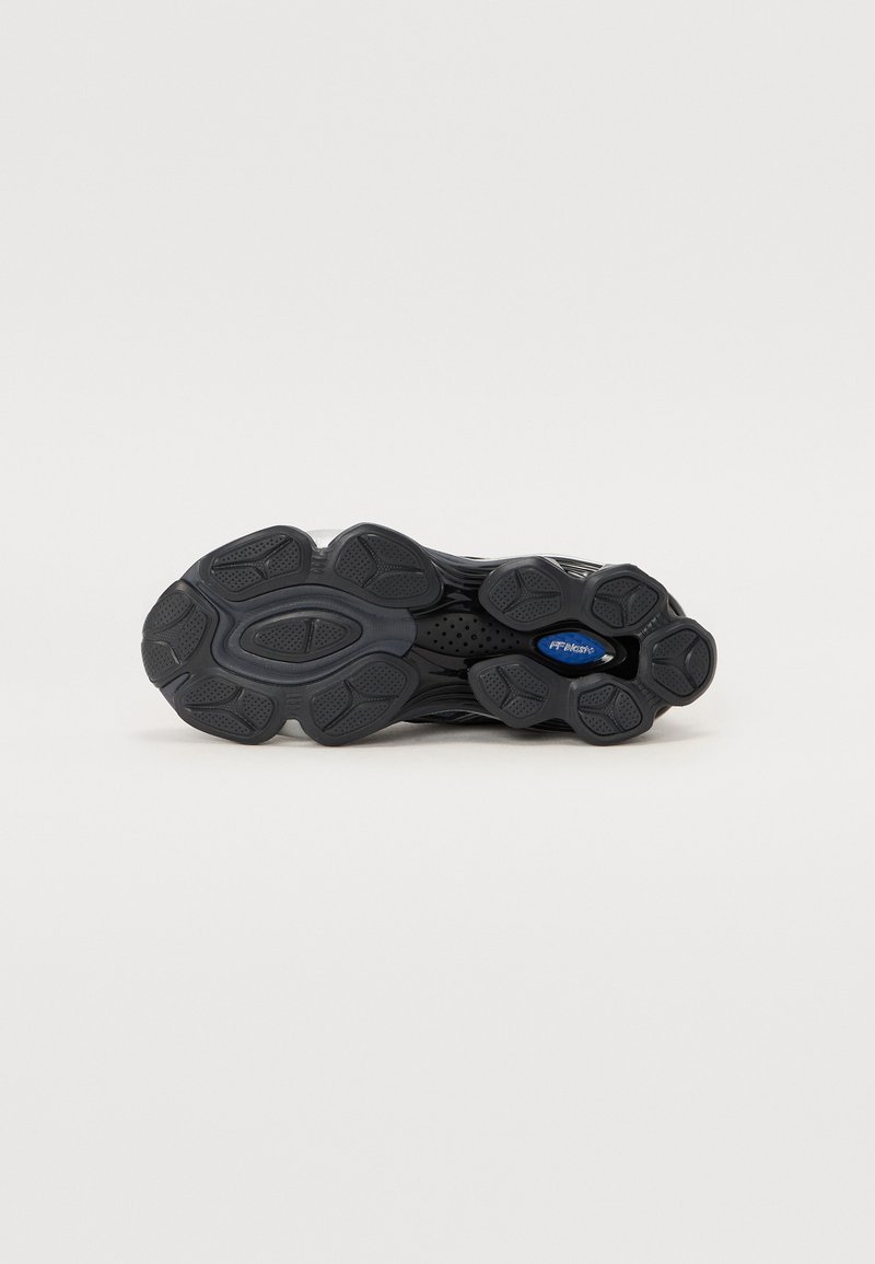Zapatilla deportiva negra con una suela de goma texturizada, que presenta un diseño ondulado, patrones de banda distintos y un acento azul en la parte inferior.