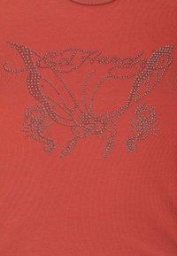 Rode T-shirt met een fitted ontwerp, voorzien van een decoratieve strassvlinder en bloemenpatroon op de voorkant. Korte mouwen en ronde halslijn.