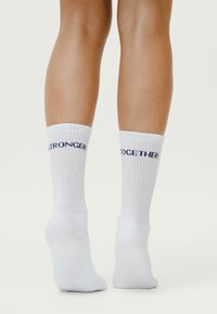 Calzini bianchi a coste con la scritta blu "STRONGER TOGETHER" stampata sul lato superiore. Realizzati in materiale morbido ed elastico per il massimo comfort.