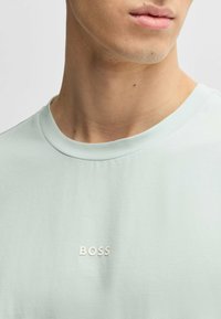 Light mint green t-shirt, cotton material, crew neck design. Features small silver "BOSS" logo on the front, smooth texture.