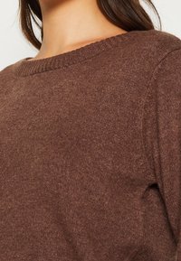 Brun stickad tröja med rund halsringning, mjuk textur och avslappnad passform. Tyget har ett subtilt, jämnt mönster.