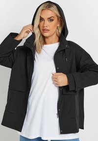 Svart vattentät jacka med huva, tryckknappar och två framfickor. Lättviktig tyg med en slät textur.