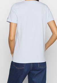 Vaaleansininen puuvillainen T-paita, jossa on lyhyet hihat, pyöreä kaula-aukko ja rento istuvuus. Yhdistettynä tummiin farkkuihin, joissa on takataskut.