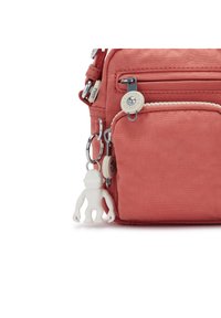 Coral fabric crossbody bag with silver hardware, front zipper pocket, and white monkey keychain accent. Features sturdy stitching and adjustable strap.