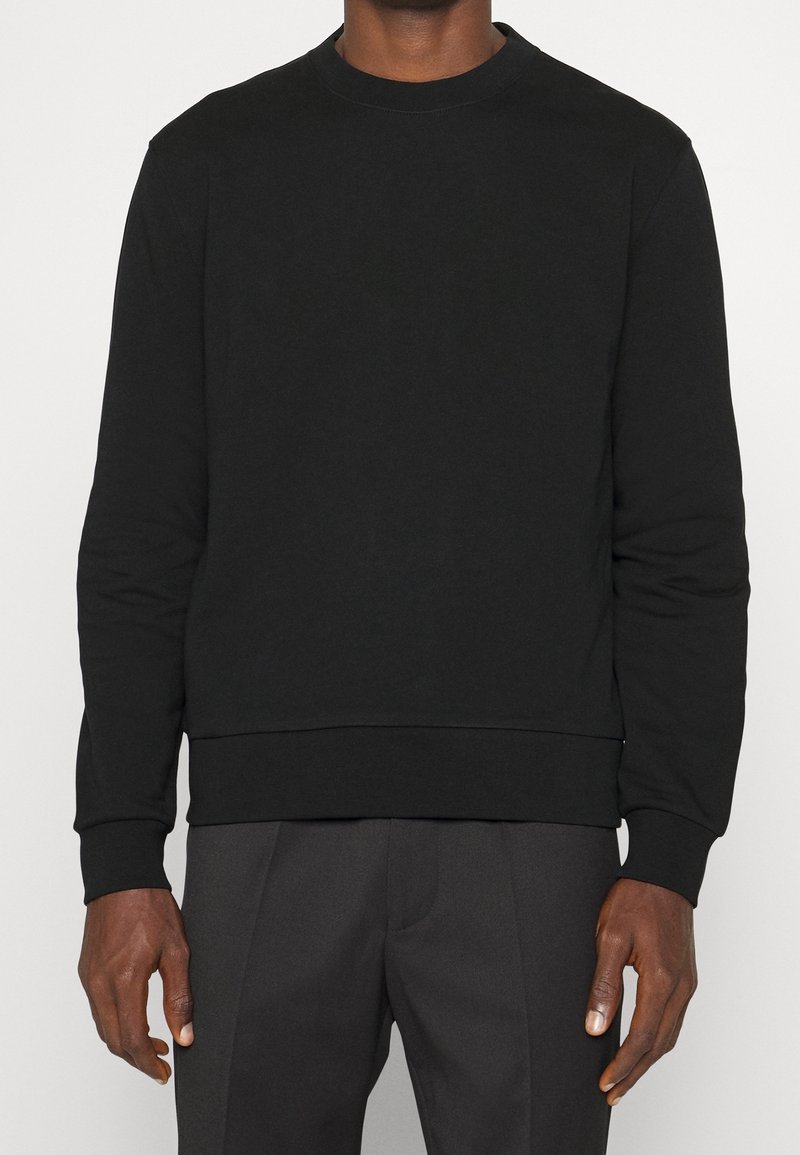 Sudadera negra de cuello redondo con mangas largas, hecha de una tela suave, que cuenta con un cuello y una cintura acanalados. Sin logotipos ni patrones visibles.