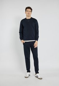 Granatowy sweatshirt i dopasowane spodnie wykonane z miękkiego materiału. Posiada długie rękawy, okrągły dekolt oraz detal z logo na klatce piersiowej.