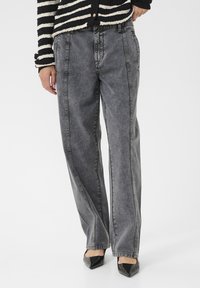 Aukštos juosmens pilkos džinsinės kelnės su laisvu siluetu, turinčios pirmosios siūlės ir blukimo efektą. Derinamos su smailėjančiomis juodomis aukštakulnėmis.