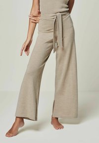 Beige weite Hosen mit strukturiertem Strick, ausgestattet mit einem gebundenen Gürtel und seitlichen Schlitzen. Glattes Material mit lockerer Passform.