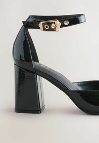 Black patent leather high-heeled sandal with a square block heel, ankle strap with gold buckle, and open toe design. Smooth, shiny texture.