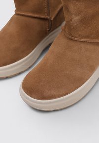 Botas de tobillo de ante marrón con punteras redondeadas. Parte superior texturizada, suelas de goma de color claro y un detalle de cremallera lateral.