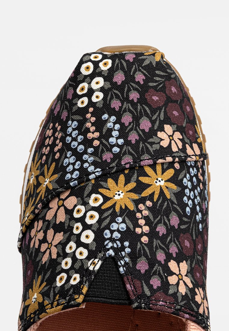 Zapatillas de tela con estampado floral, que presentan una parte superior de lona negra adornada con flores multicolores, un tejido texturizado y una suela de goma.
