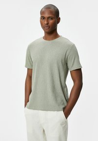 Kortærmet, lysegrøn t-shirt med tekstureret stof og rund halsudskæring, parret med cremefarvede bukser.