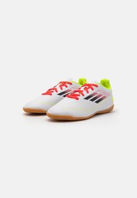 Scarpe da calcio bianche con lacci rossi, strisce nere e dettagli verde neon. Superficie testurizzata con una suola in gomma naturale e forma aerodinamica.