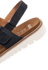 Mørkeblå ruskindsandaler med flad hvid gummisål, justerbar rem og blød brun indersål med mærke.