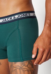 Green boxer briefs with a navy elastic waistband featuring "JACK & JONES" branding. Smooth texture and fitted design with visible stitching details.