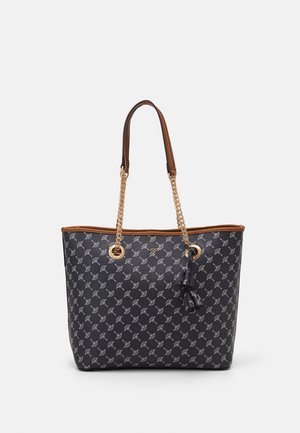 Zwarte tote met wit geometrisch patroon, bruine afwerking, gouden kettinghengsels en decoratieve kwastjes die aan één hengsel hangen.