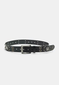 Zwarte lederen riem met zilveren gesp, versierd met ronde metalen studs en bloemenpatronen, plat gelegd op een witte achtergrond.