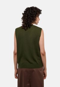 Pull sans manches vert olive en tricot avec un col rond et un ourlet côtelé. Texture lisse et coupe décontractée, associé à une jupe marron.