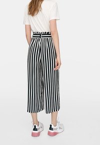 Culottes rayées noir et blanc avec une taille haute et des passants de ceinture, associées à une chemise blanche à manches courtes et des baskets blanches sportives.