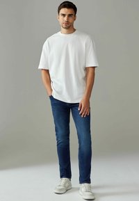 T-shirt oversize blanche à manches courtes, associée à un jean bleu foncé et des baskets blanches. Design simple, texture douce et coupe décontractée.