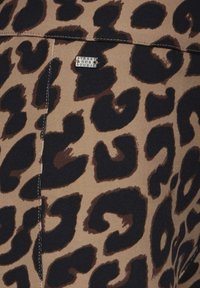 Hnědá látka s vzory v podobě černých leopardích skvrn, s viditelným prošitím a malou stříbrnou štítkem s nápisem "STREET ON THE STUDIO."