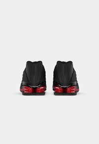 Par crnih Nike Shox tenisica prikazanih s leđa s crvenim jastučićem u srednjem dijelu i crnim potplatima na jednobojnoj bijeloj pozadini.