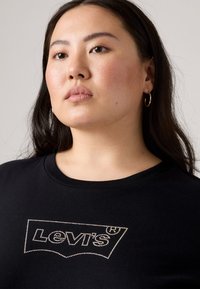 T-shirt noir en coton avec un design de logo Levi's en strass brillants. L'encolure est ronde et le tissu a une texture lisse.
