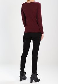 Top burdeos de manga larga, diseño ajustado, textura suave. Combinado con unos jeans ajustados negros y botas de tacón negro con ataduras.