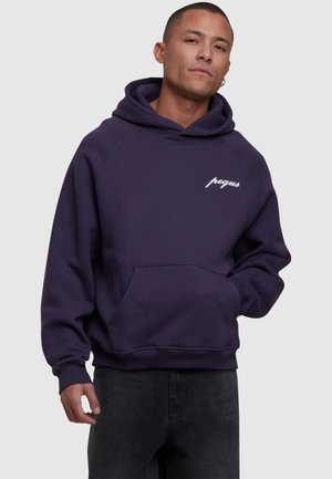 Sudadera morada con bolsillo frontal y texto "pequs" en blanco. Presenta una capucha con cordón y puños acanalados. Material suave de mezcla de algodón.
