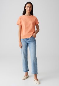 T-shirt in cotone arancione chiaro con maniche arrotolate, abbinata a jeans dritti blu chiaro e scarpe slip-on color crema.