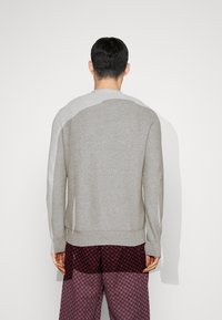 Grå stickad tröja med långa ärmar, rund halsringning och ribbade ärmmuddar. Bärs med mönstrade byxor. Enkel textur och diskret design.