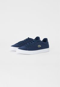 Zapatillas de lona navy con suelas de goma blanca, que cuentan con una superficie texturizada, punta redonda y un logo verde bordado en el costado.