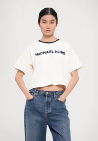T-shirt bianco a maniche corte con colletto blu navy e testo "MICHAEL KORS" in blu navy. Abbinato a jeans blu in denim dal taglio morbido. Design semplice e casual.