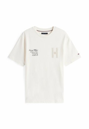 Biała bawełniana koszulka z teksturowanym logo „H” na klatce piersiowej, tekstem marki po lewej stronie oraz małym akcentem flagi na rękawie.