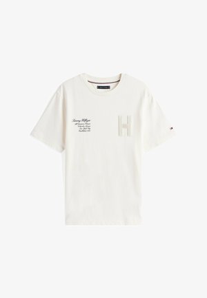 Biała bawełniana koszulka z teksturowanym logo „H” na klatce piersiowej, tekstem marki po lewej stronie oraz małym akcentem flagi na rękawie.