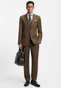 Completo marrone su misura con due bottoni, rever a lancia e tasche a patta. Camicia da uomo azzurro chiaro e cravatta texturizzata. Borsa in pelle marrone e scarpe.