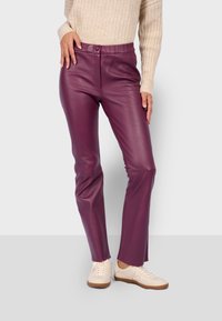 Pantalones de cuero morado con una textura suave, diseño ajustado y cierre de botón en la parte delantera. Combinados con zapatillas de color crema.