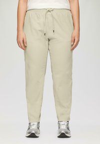 Hellbeige Jogginghosen mit elastischem Bund und Kordelzug. Hergestellt aus weichem Stoff mit slim fit, kombiniert mit silbernen Sportschuhen.