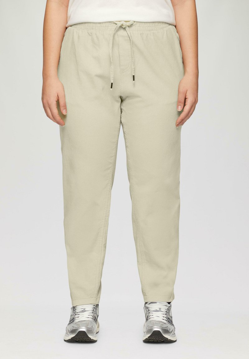 Hellbeige Jogginghosen mit elastischem Bund und Kordelzug. Hergestellt aus weichem Stoff mit slim fit, kombiniert mit silbernen Sportschuhen.