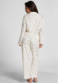 Lichtbeige pyjama set met zwarte bloemenpatronen, bestaande uit een colbert met lange mouwen en bijpassende wijde broek van een zachte stof.