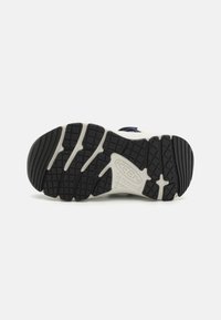 Sola de borracha preta com sulcos profundos para tração, apresentando uma entressola branca e detalhes de design em azul e amarelo.