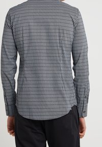 Tröja med långa ärmar i svartvitt mönstrat tyg med vertikala ränder och knäppta manschetter; slät textur och skräddarsydd passform.