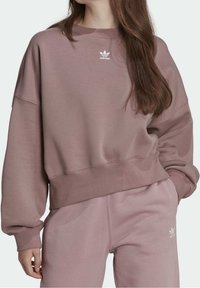 Överdimensionerad, dammig rosa sweatshirt i mjukt tyg med ribbade muddar och nederkant; har en liten vit Adidas-logotyp på bröstet.