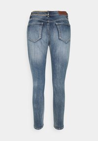 Jeans de denim ajustados en lavado azul claro, con una cintura de altura media, cinco bolsillos y una tela texturizada con sutiles detalles de desgaste y desteñido.