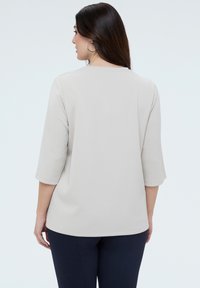 Lichtgrijs topje met driekwartmouwen en geborduurd bloemenpatroon op de mouwen. Gladde stof, losse pasvorm en ronde halslijn.