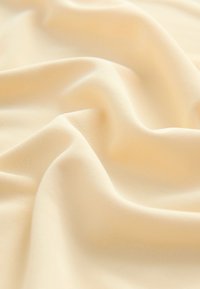 Tissu doux et léger de couleur crème pâle, présentant une texture lisse avec un tombé subtil et des plis délicats.