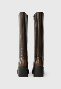 Par de botas altas de couro castanho escuro com saltos quadrados e zíperes nas costas, vistas de trás sobre um fundo branco.