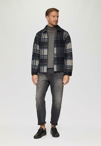 Geruite flanellen jasje in marineblauw, grijs en wit; slim-fit grijze jeans; zwarte sneakers; ronde hals grijze coltrui; casual stijl, geen zichtbare hardware.