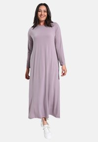 Langes lilafarbenes Kleid mit langen Ärmeln, einem schlichten Rundhalsausschnitt und seitlichen Schlitzen, kombiniert mit weißen Sneakers. Glattes Material, lockere Passform.