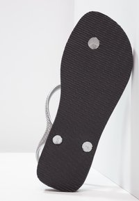 Hopeatarjonnan hopeiset hihnasandaalit, joissa on teksturoitu musta kumipohja; joissa on kaksi metallista niittiä lisäyksinä.